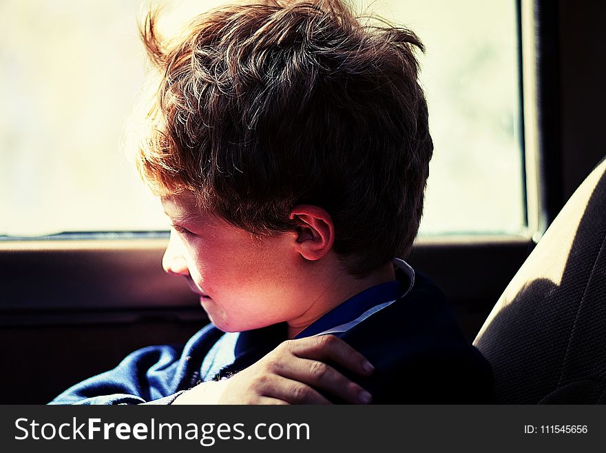 Boy in Blue Jacket Sitting Next to Vehicle Window