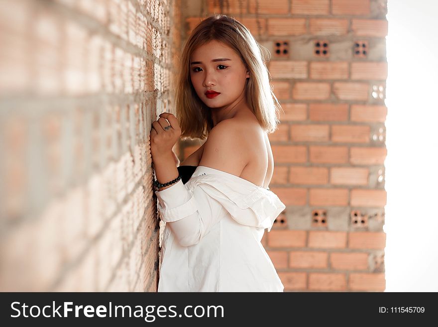 Shallow Focus Photography of Woman in White Top Beside Red Brick Wall