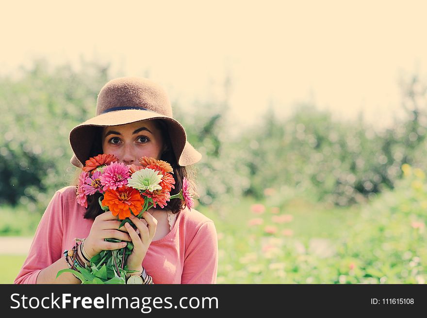 Woman Wearing Hat and Holding Flowers Surrounded by Plants