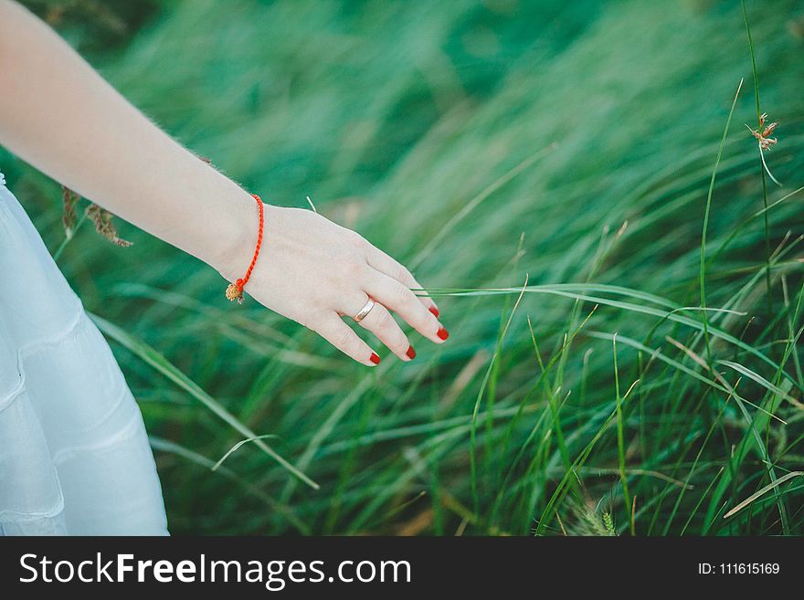 Woman Wearing White Skirt, Orange Bracelet, and Red Manicure Beside Green Grass