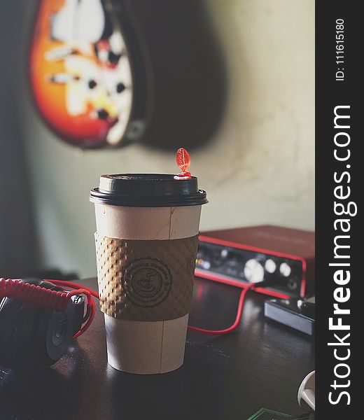White and Brown Labeled Plastic Coffee Cup on Brown Tabletop Near Black Multimedia Player