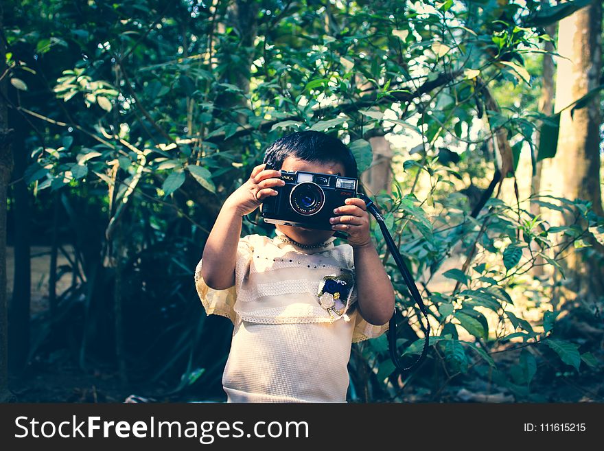 Boy Holding Black Flash Camera Near Green Leaf Plants