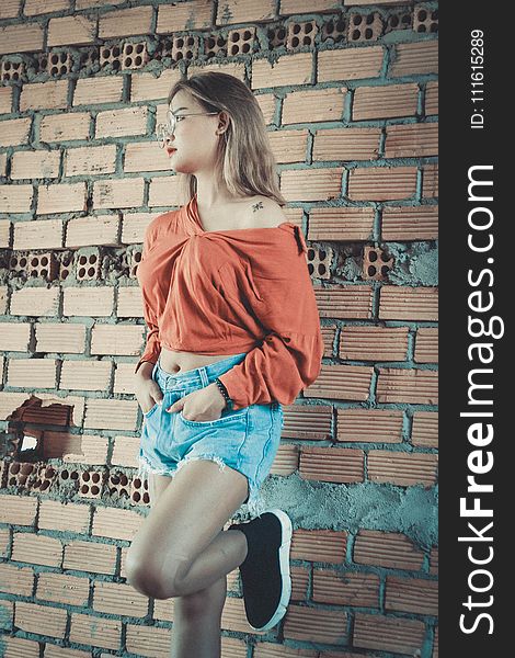 Woman Wearing Brown Long-sleeved Blouse and Blue Denim Short Shorts Standing Behind Brown Brick Wall