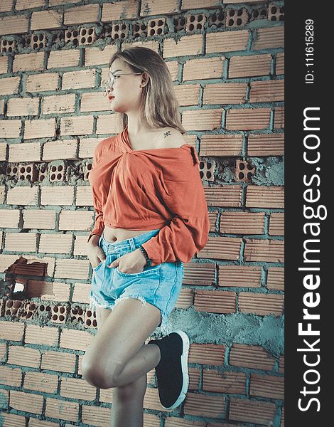 Woman Wearing Brown Long-sleeved Blouse And Blue Denim Short Shorts Standing Behind Brown Brick Wall