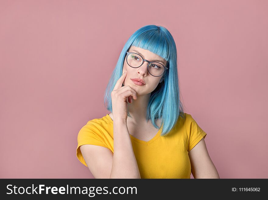 Beautiful pensive young woman with blue color dyed hair with hipster style spectacles thinking in front of pastel studio background. Beautiful pensive young woman with blue color dyed hair with hipster style spectacles thinking in front of pastel studio background.