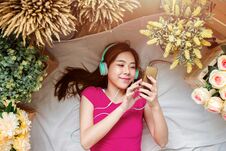 Happy Young Woman Laying On The Floor To Listening Music Via Smart Phone. Girl Relaxing In Cozy Place, Surrounded By Flower, Top Stock Photography