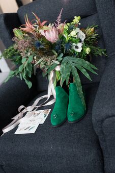 Rich Green Wedding Bouquet With Pink Ribbons On The Grey Armchair. Green Bridal Shoes, And A Wedding Complimentary Lying Near The Royalty Free Stock Photography