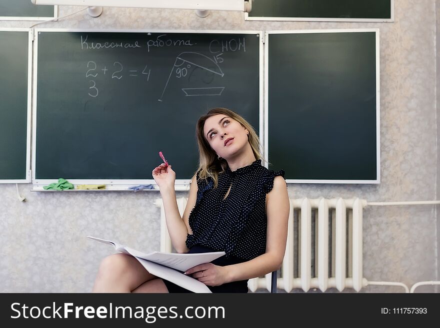 Strict young blonde teacher sits on a chair crossing her legs and dreamy looks at the ceiling