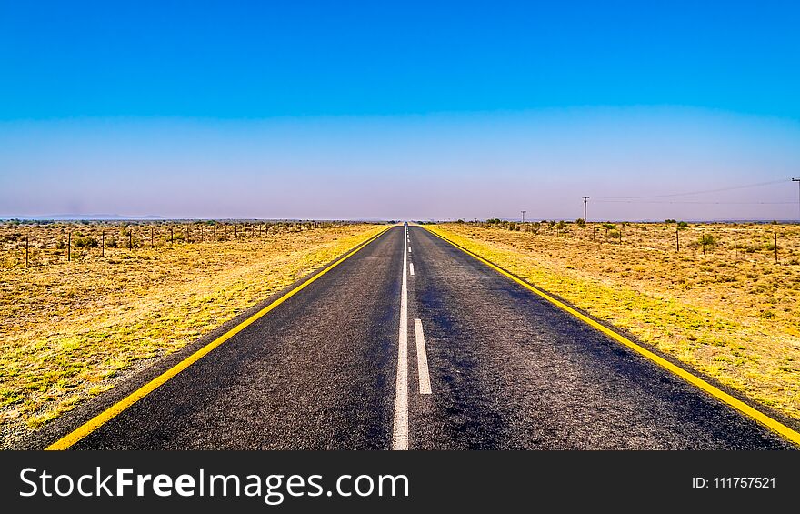 Long Straight Road through the Endless wide open landscape of the semi desert Karoo Region in Free State and Eastern Cape provinces in South Africa under blue sky