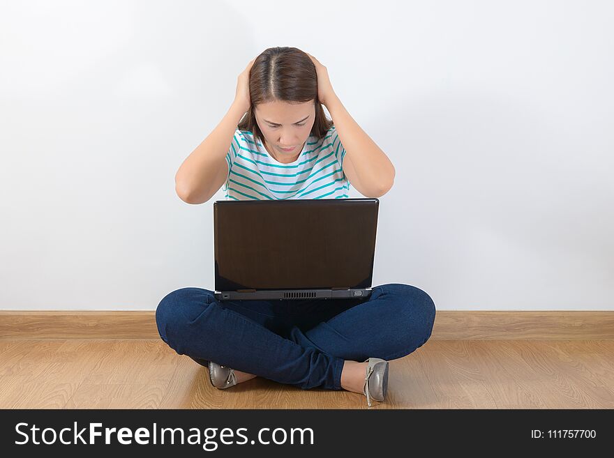 Tired teen woman with laptop sitting on the wooden floor