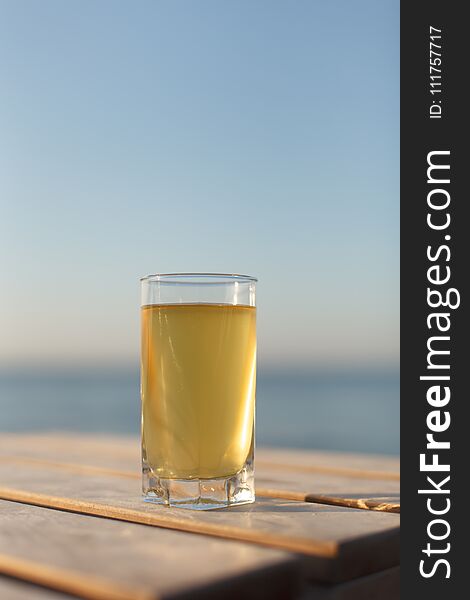 Glass of cold drink on sunbed or wooden table on sea and sky background. Vertical image with copyspace. Glass of cold drink on sunbed or wooden table on sea and sky background. Vertical image with copyspace