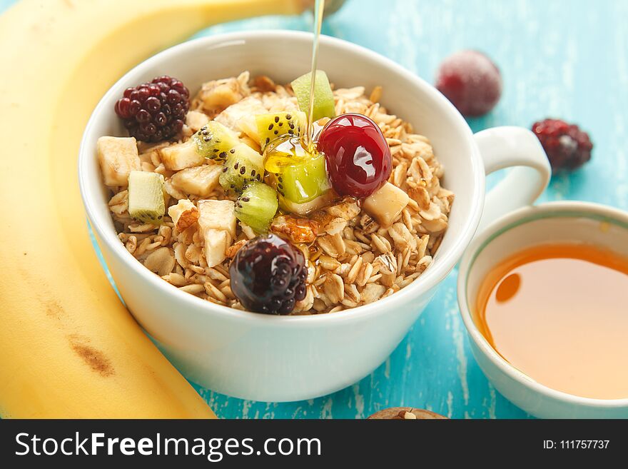 Cup of oat flakes with cherry, kiwi, blackberry, egg, walnut and honey in small cup on a turquoise wooden table.