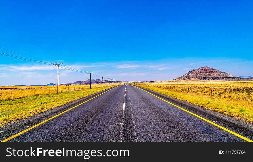 Long Straight Road through the Endless wide open landscape of the semi desert Karoo Region in Free State and Eastern Cape provinces in South Africa under blue sky