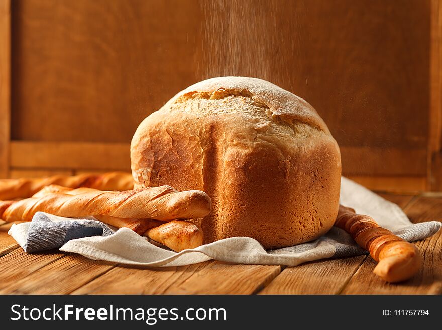 Flour is pouring on loaf and four french baguettes. Bread lay on napkin on rustic wooden table. Concept of homemade pastry or bakery. Flour is pouring on loaf and four french baguettes. Bread lay on napkin on rustic wooden table. Concept of homemade pastry or bakery