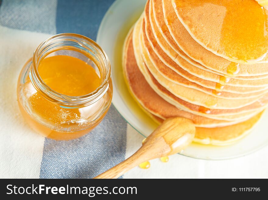 Stack of pancakes with pouring honey on plate with wooden spoon and jar with honey. Concept of tasty breakfast, close-up view. Selective focus. Stack of pancakes with pouring honey on plate with wooden spoon and jar with honey. Concept of tasty breakfast, close-up view. Selective focus