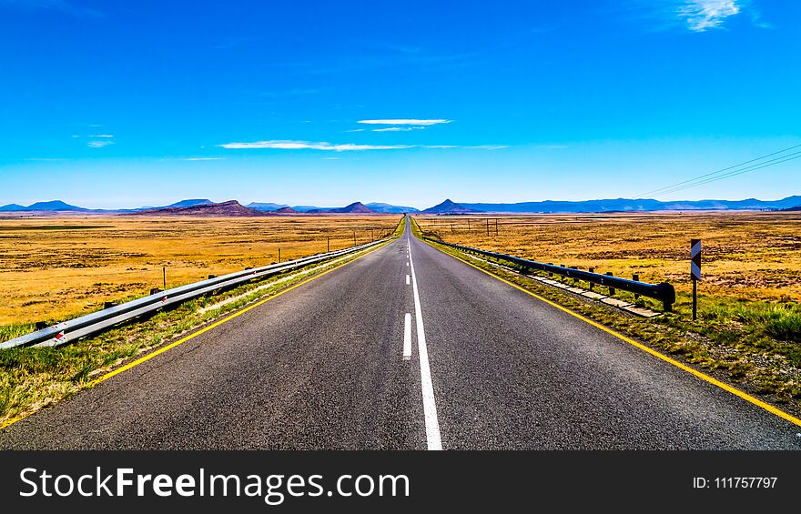 Long Straight Road through the Endless wide open landscape of the semi desert Karoo Region in Free State and Eastern Cape provinces in South Africa under blue sky