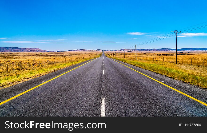 Long Straight Road through the Endless wide open landscape of the semi desert Karoo Region in Free State and Eastern Cape provinces in South Africa under blue sky