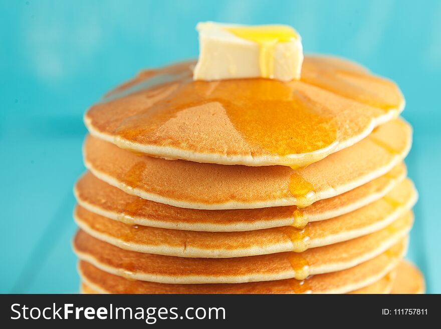 Stack of pancakes with honey and piece of butter on plate which stands on napkin on blue wooden table. Copyspace. Concept of shrovetide treats. Selective focus. Stack of pancakes with honey and piece of butter on plate which stands on napkin on blue wooden table. Copyspace. Concept of shrovetide treats. Selective focus