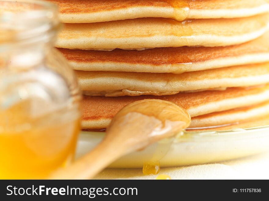 Close Up Of Stack Of Pancake With Pouring Honey, Wooden Spoon And Jar Of Honey