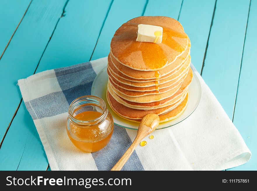 Stack of pancakes with pouring honey on plate with wooden spoon and jar with honey. Concept of tasty breakfast, close-up view. Selective focus. Stack of pancakes with pouring honey on plate with wooden spoon and jar with honey. Concept of tasty breakfast, close-up view. Selective focus