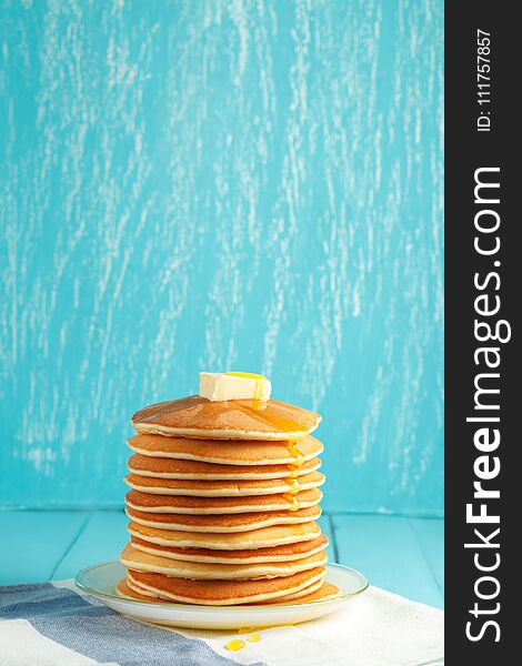 Stack of pancakes with honey and piece of butter on plate which stands on napkin on blue wooden table. Copyspace. Concept of shrovetide treats or tasty food. Selective focus. Stack of pancakes with honey and piece of butter on plate which stands on napkin on blue wooden table. Copyspace. Concept of shrovetide treats or tasty food. Selective focus