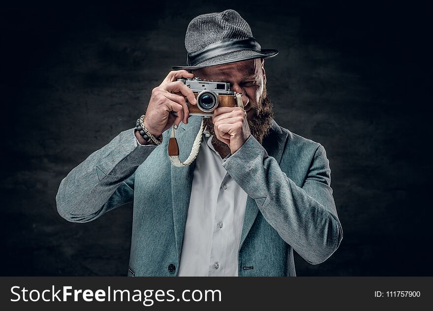 A man dressed in a grey jacket and felt hat holds an SLR photo c