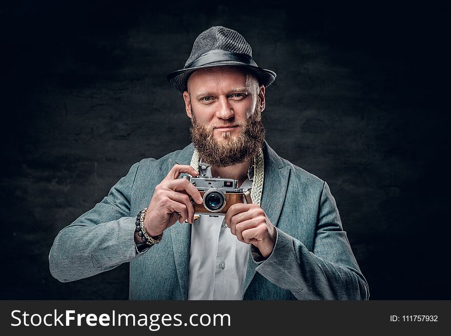 A stylish bearded hipster male dressed in a grey jacket and felt hat holds an SLR photo camera. A stylish bearded hipster male dressed in a grey jacket and felt hat holds an SLR photo camera.