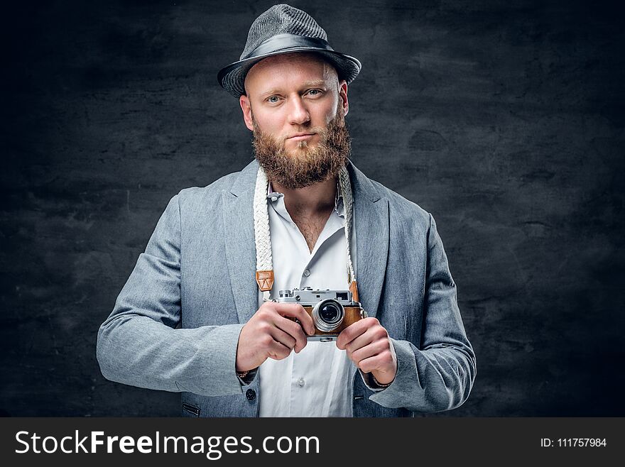 Studio portrait of bearded photographer dressed a suit and felt hat holds an old vintage SLR photo camera. Studio portrait of bearded photographer dressed a suit and felt hat holds an old vintage SLR photo camera.