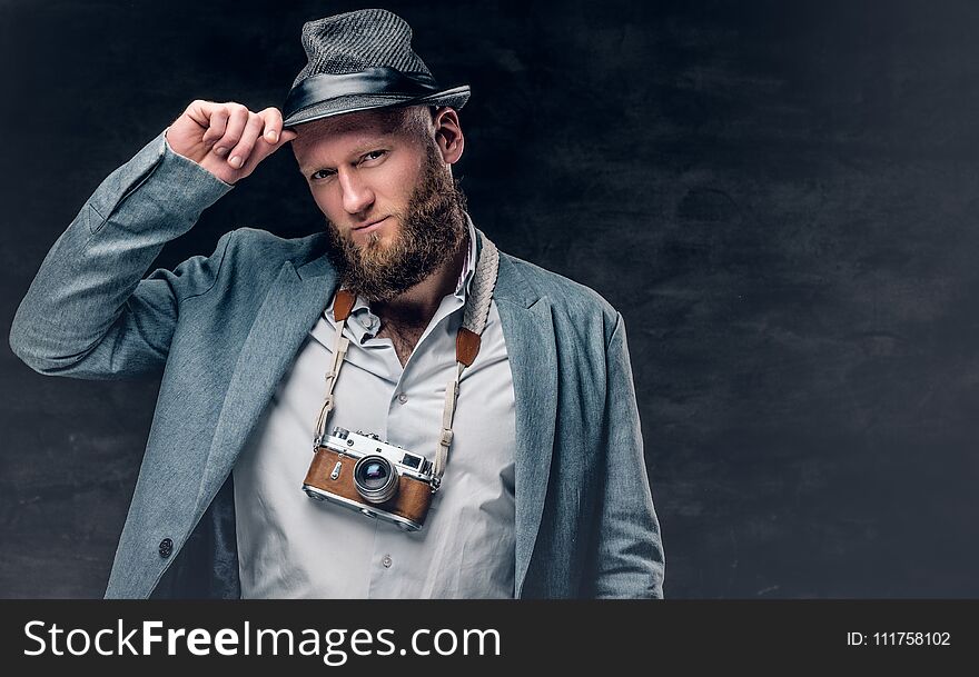 Studio portrait of bearded photographer dressed a suit and felt hat holds an old vintage SLR photo camera. Studio portrait of bearded photographer dressed a suit and felt hat holds an old vintage SLR photo camera.