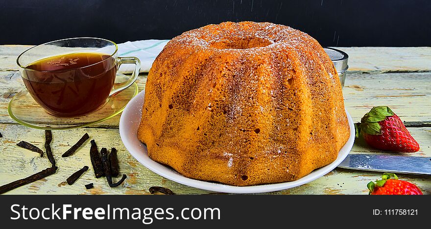 Old fashioned sand cake with cup of black tea and pieces of vanilla on wooden background. Egg-yolk sponge cake on rustic white background. Pouring sugar on sand cake.