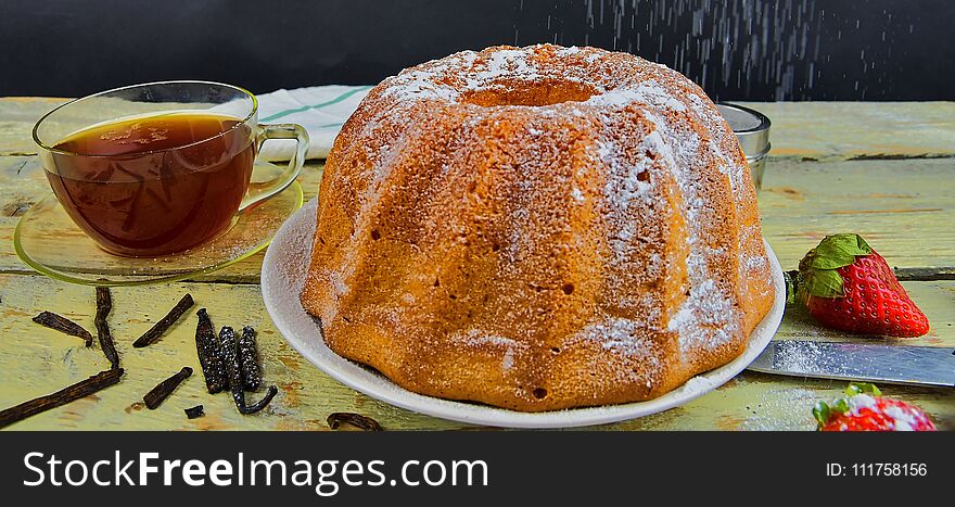 Old fashioned sand cake with cup of black tea and pieces of vanilla on wooden background. Egg-yolk sponge cake on rustic white background. Pouring sugar on sand cake.