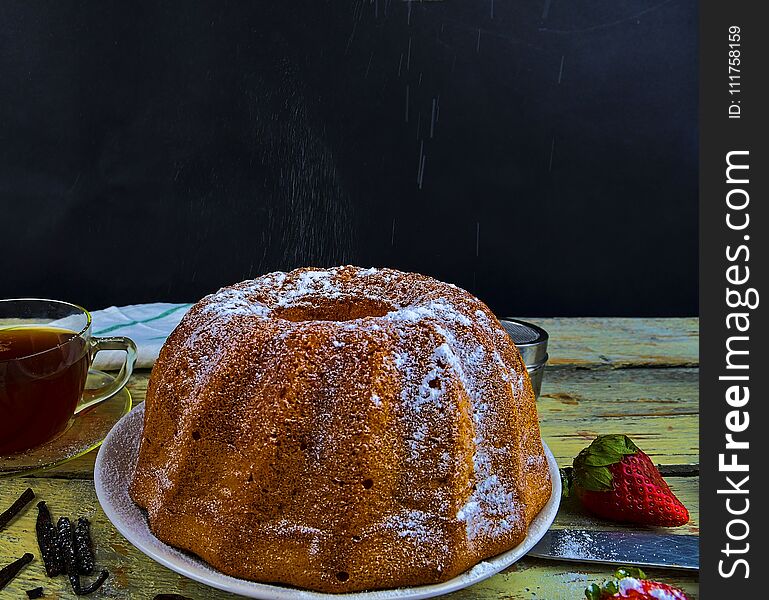 Old fashioned sand cake with cup of black tea and pieces of vanilla on wooden background. Egg-yolk sponge cake on rustic white background. Pouring sugar on sand cake.