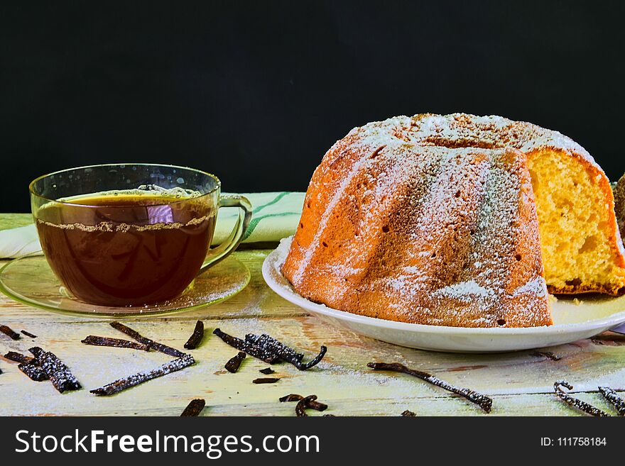 Old fashioned sand cake with cup of black tea and pieces of vanilla on wooden background. Egg-yolk sponge cake on rustic white background