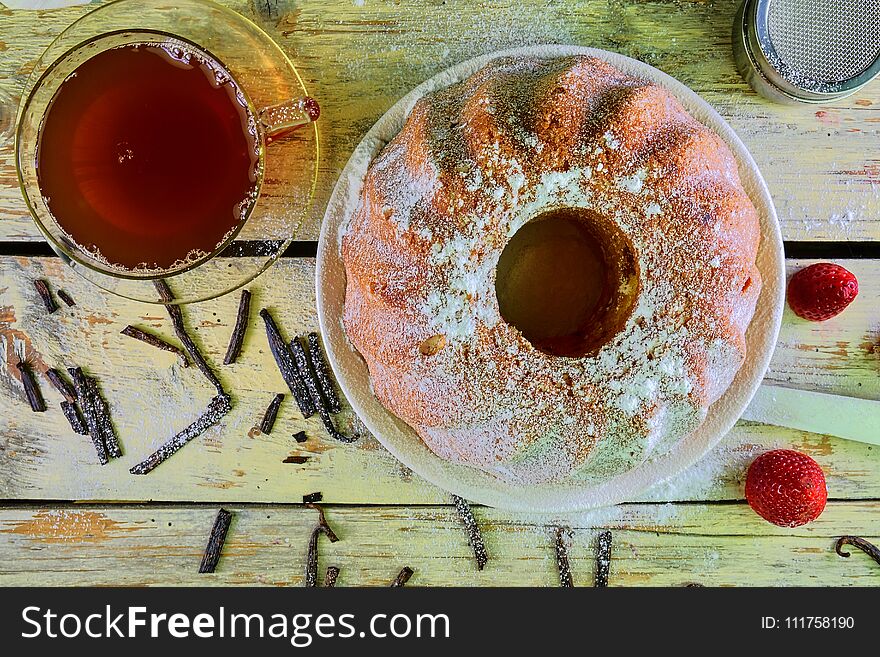 Old fashioned sand cake with cup of black tea and pieces of vanilla on wooden background. Egg-yolk sponge cake with stawberries on rustic white background. Top view. Flat design.