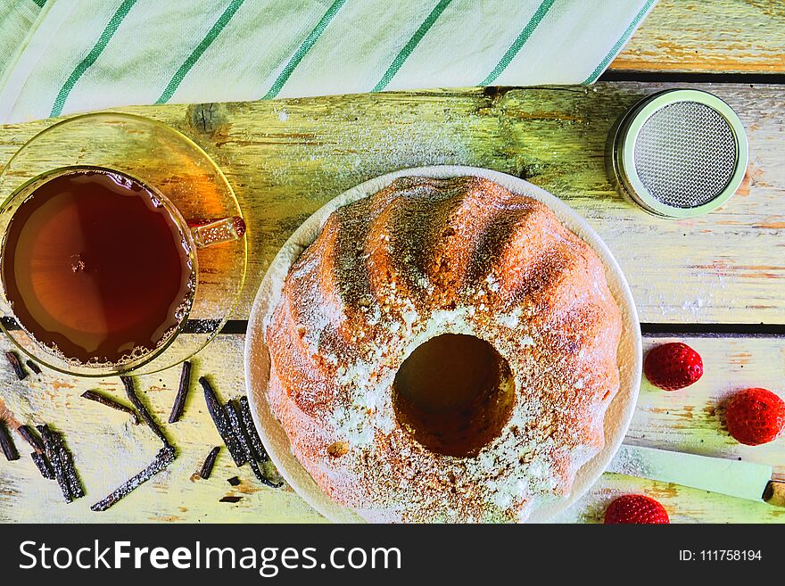 Old fashioned sand cake with cup of black tea and pieces of vanilla on wooden background. Egg-yolk sponge cake with