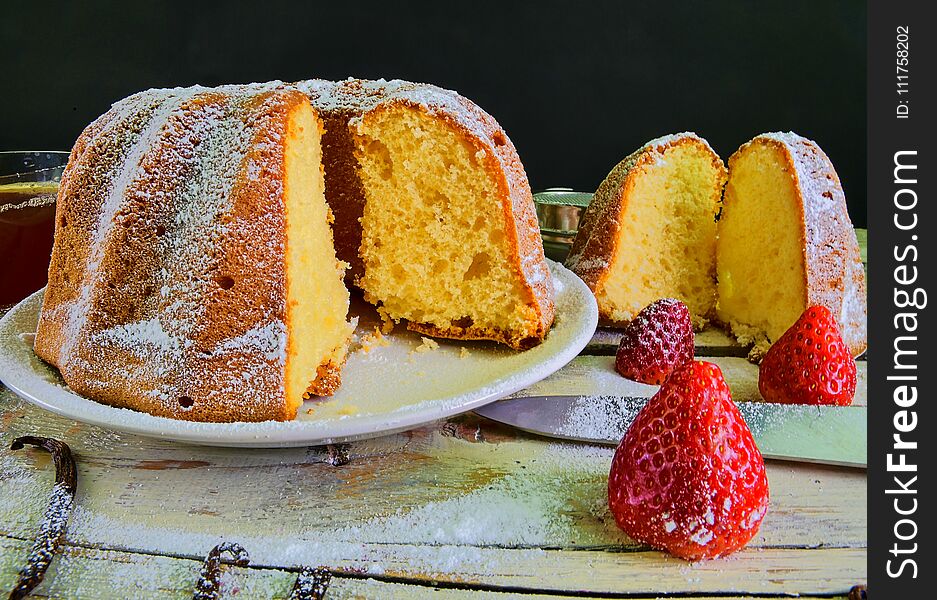 Old fashioned sand cake with cup of black tea and pieces of vanilla on wooden background. Egg-yolk sponge cake with stawberries on rustic white background.