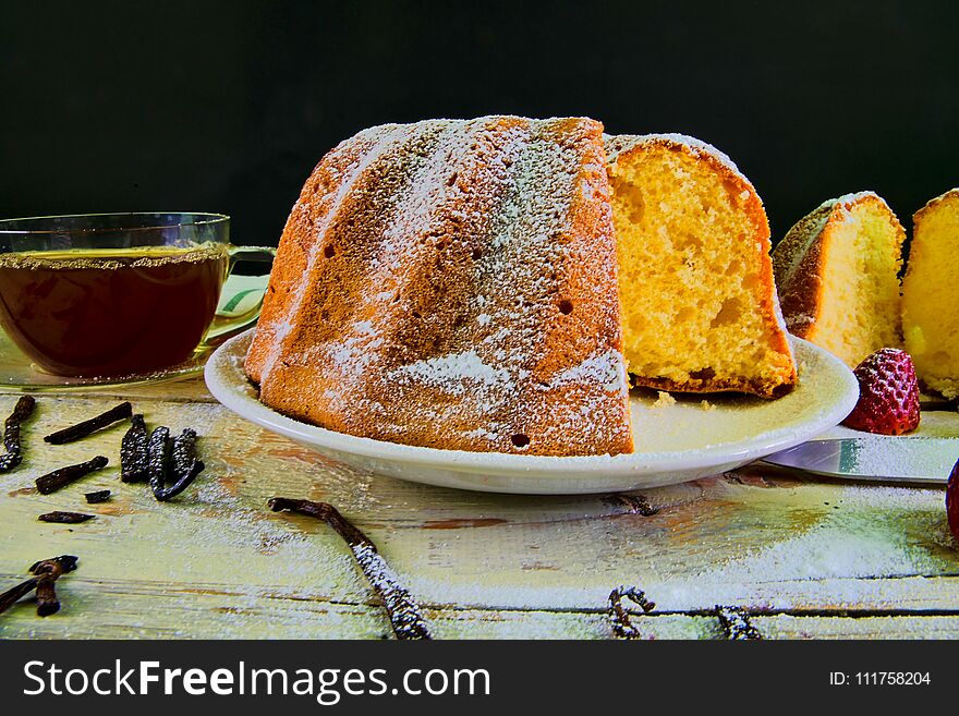 Old fashioned sand cake with cup of black tea and pieces of vanilla on wooden background. Egg-yolk sponge cake with stawberries on rustic white background