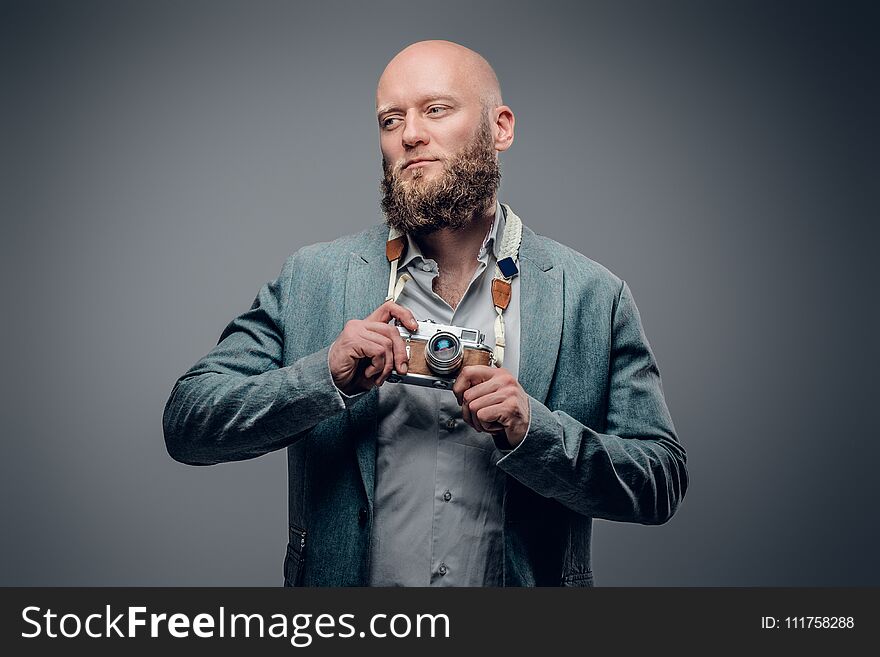 A stylish bearded hipster male dressed in a grey jacket and felt hat holds an SLR photo camera. A stylish bearded hipster male dressed in a grey jacket and felt hat holds an SLR photo camera.