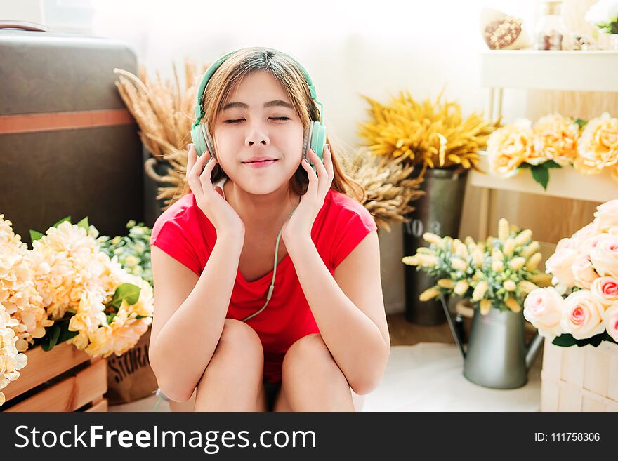 Happy Young Woman Listening Music From Smart Phone in Cozy House, Surrounded by Flower and Sunlight from the back