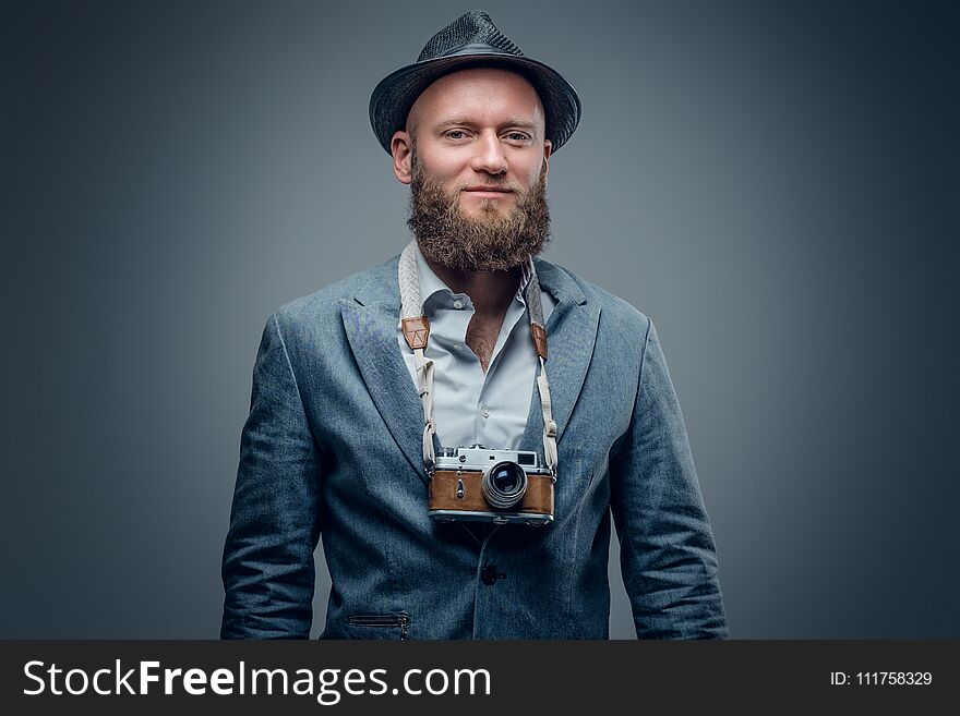 Studio portrait of bearded photographer dressed a suit and felt hat holds an old vintage SLR photo camera. Studio portrait of bearded photographer dressed a suit and felt hat holds an old vintage SLR photo camera.