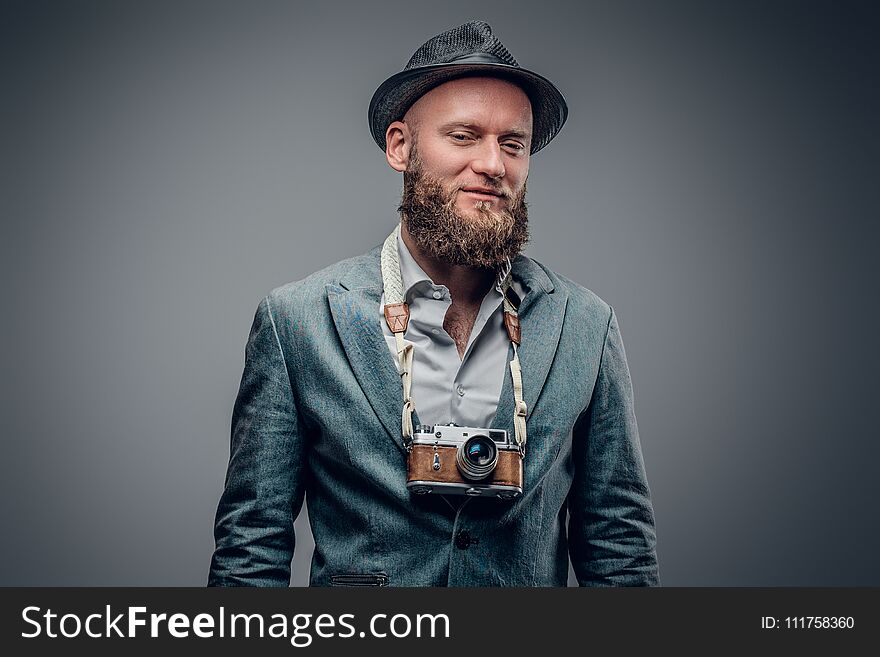 A stylish bearded hipster male dressed in a grey jacket and felt hat holds an SLR photo camera. A stylish bearded hipster male dressed in a grey jacket and felt hat holds an SLR photo camera.