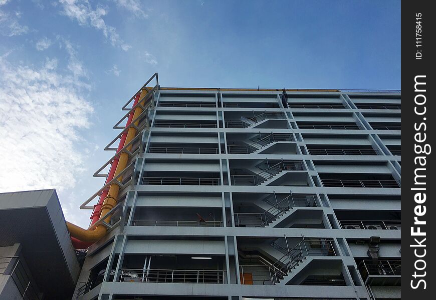 Architecture building, It has stair every floor. orange and yellow pipe side the building. cirrocumulus clouds and blue sky. industrial heathy and medical. Architecture building, It has stair every floor. orange and yellow pipe side the building. cirrocumulus clouds and blue sky. industrial heathy and medical