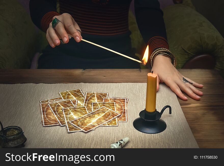 Tarot cards on fortune teller desk table. Future reading. Woman lights a candle by matches. Tarot cards on fortune teller desk table. Future reading. Woman lights a candle by matches.