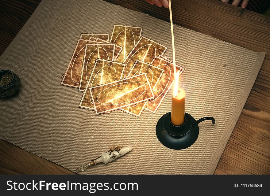 Tarot cards on fortune teller desk table. Future reading. Woman lights a candle by matches. Tarot cards on fortune teller desk table. Future reading. Woman lights a candle by matches.