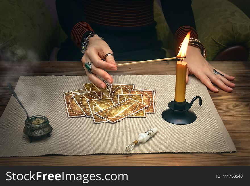 Tarot cards on fortune teller desk table. Future reading. Woman lights a candle by matches. Tarot cards on fortune teller desk table. Future reading. Woman lights a candle by matches.