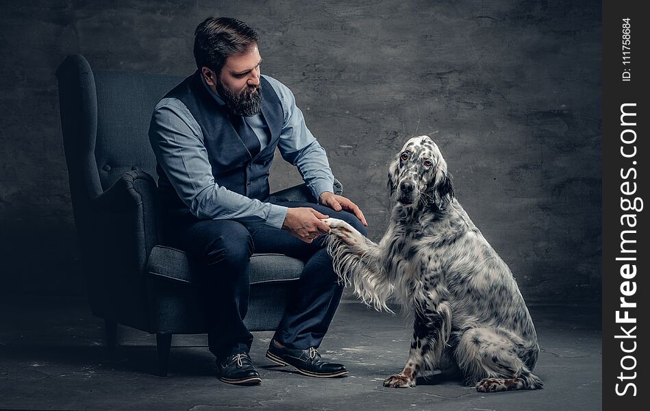 Portrait of stylish bearded male sits on a chair and the Irish setter dog.