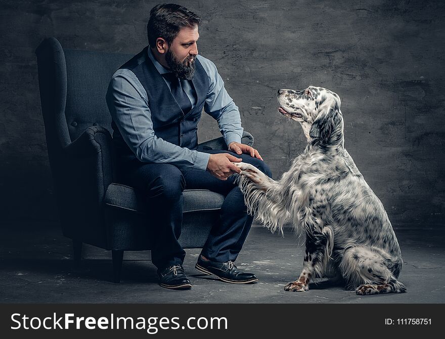 Stylish bearded male sits on a chair and the Irish setter dog.