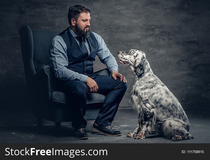 Stylish bearded male sits on a chair and the Irish setter dog.