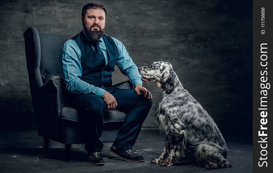 Stylish bearded male sits on a chair and the Irish setter dog.