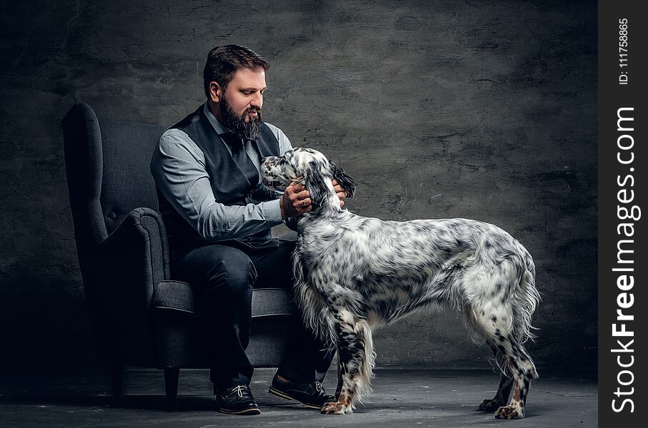 Portrait of stylish bearded male sits on a chair and the Irish setter dog.